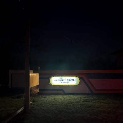 A brightly lit sign reading Sprint Kart Raceway is attached to a building in St. Charles, illuminating the structure at night. The area around this popular go karts spot remains mostly dark, with only a grassy patch visible nearby.