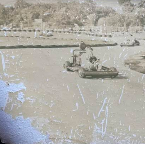 A vintage, scratched photo shows a person driving a go-kart on an outdoor track at Boschertown Go Karts in St. Charles, with trees and fencing visible in the background.