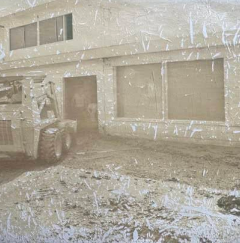 A scratched, faded photo shows a construction vehicle in front of a St. Charles building with large windows and a garage-style door, surrounded by dirt and debris—perhaps once the site of Boschertown Go Karts.