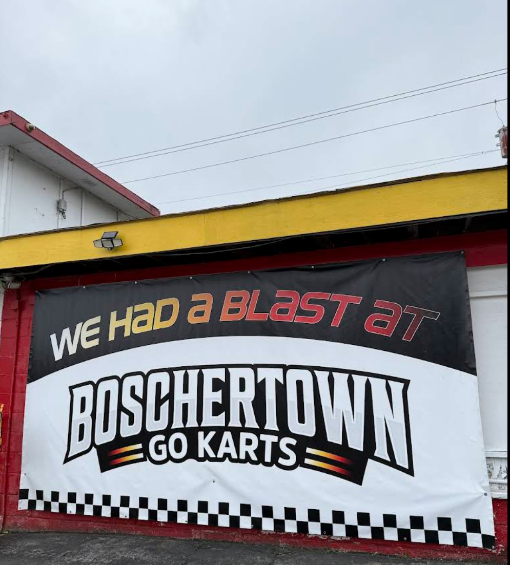 A large banner on a building in St. Charles reads, WE HAD A BLAST AT BOSCHERTOWN GO KARTS, in bold letters with a checkered pattern at the bottom. The building is painted red, yellow, and white.